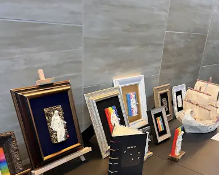 Display of framed artwork and sculptures on a table against a tiled wall.