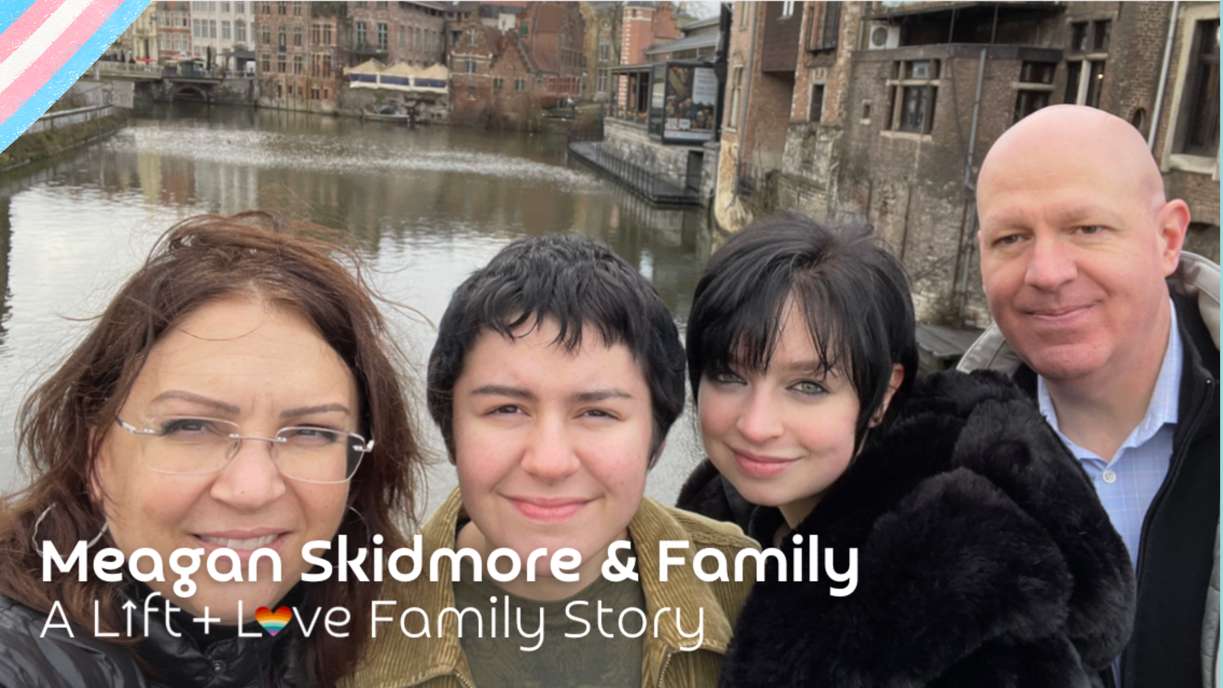 A family of four taking a selfie outdoors by a river in an urban area with historic buildings, including two women and two men, smiling at the camera.