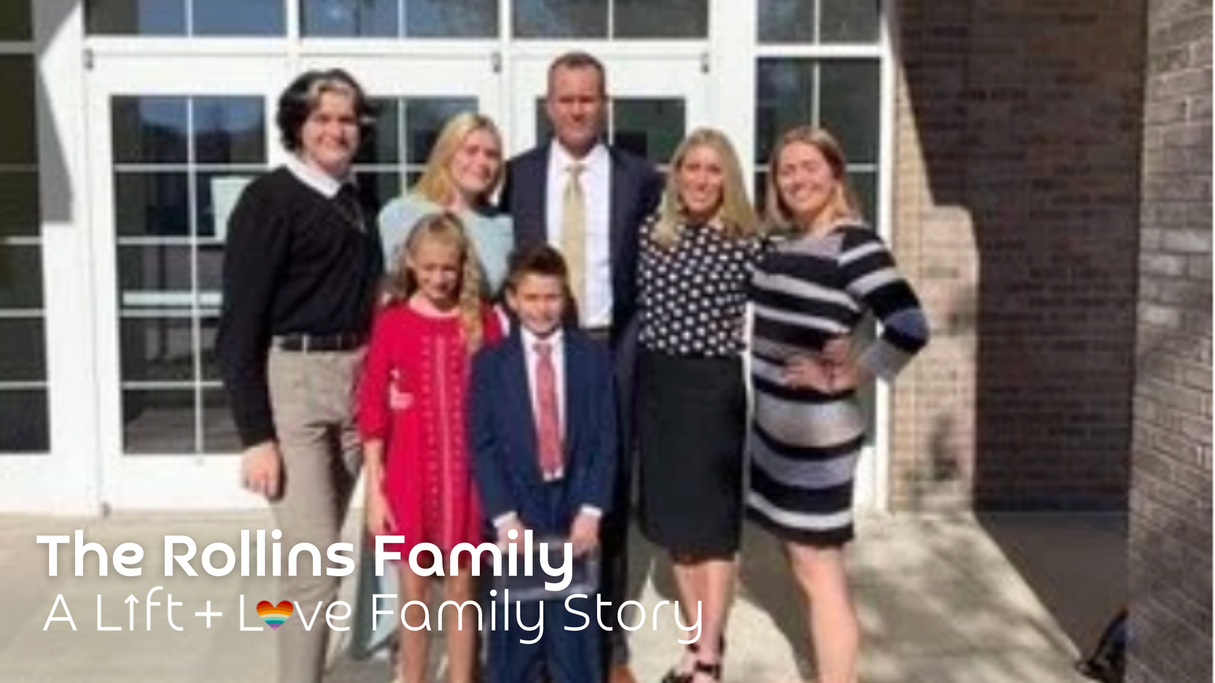 The Rollins family standing outside in front of a building with glass doors. There are seven members, including adults and children, dressed in business and casual attire, smiling at the camera.