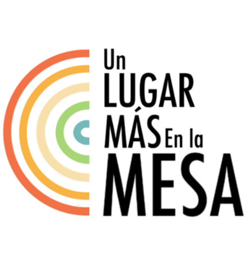A colorful abstract half-circle design on the left with concentric arcs in shades of red, orange, yellow, beige, and green. To the right, bold black text reads, "Un LUGAR MÁS En la MESA."