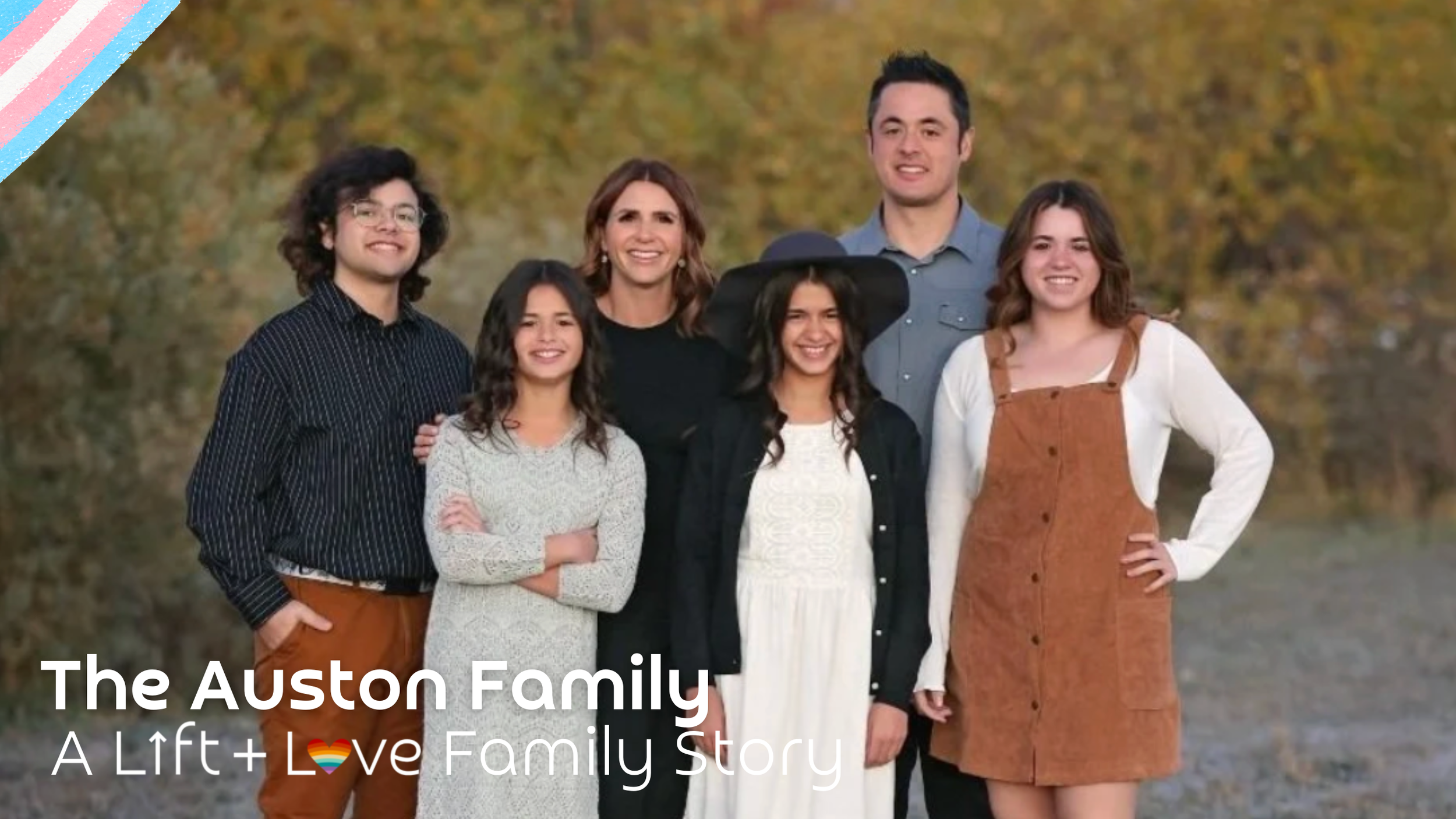 A happy family of seven standing outdoors with autumn foliage in the background, smiling at the camera.
