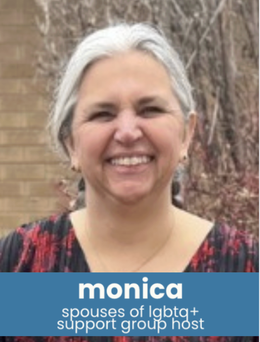 A woman with gray hair smiling outdoors, wearing a black and red patterned top, with leafless trees and a brick wall in the background.