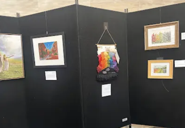 Art gallery display with framed paintings and a colorful woven wall hanging on black walls.