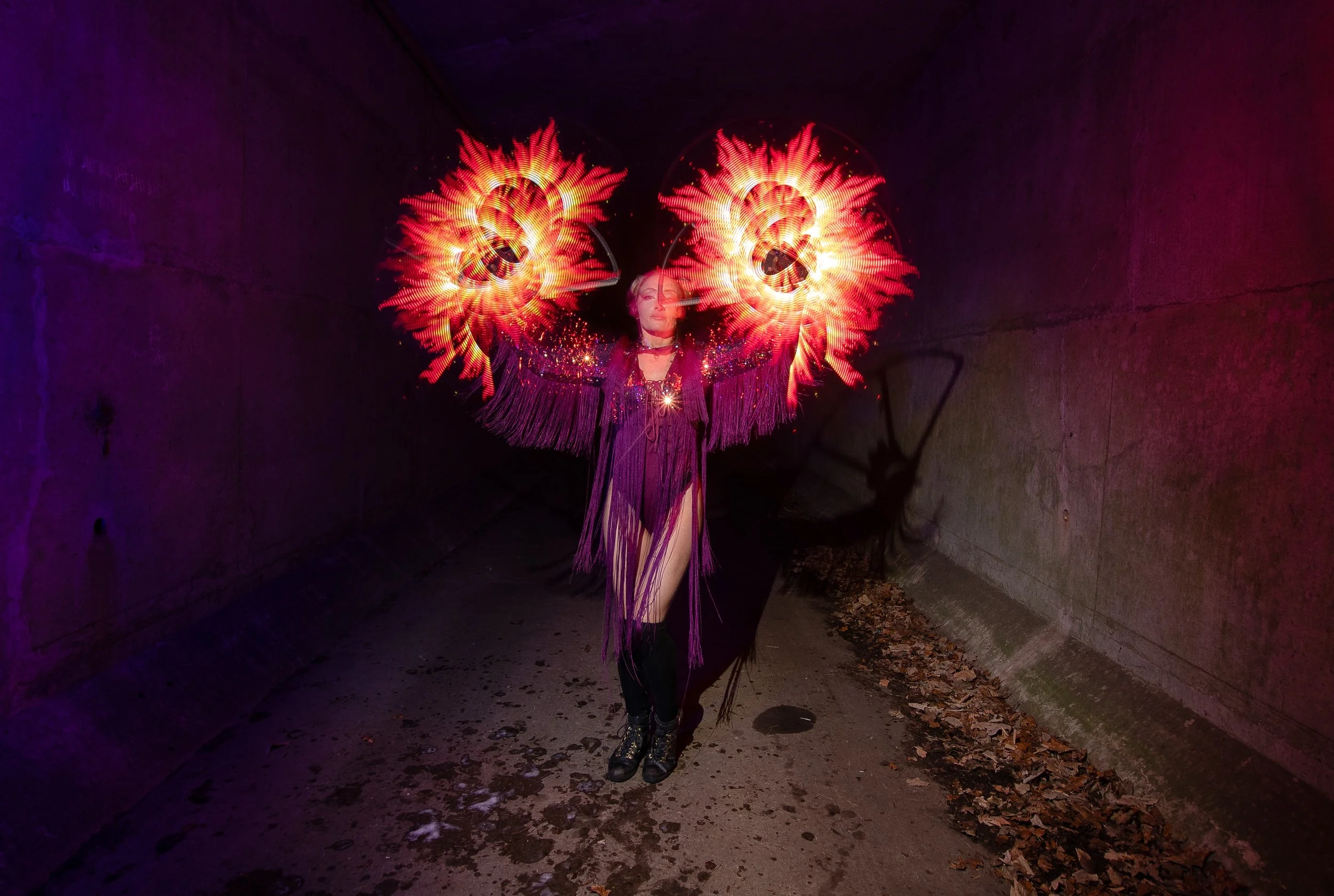 A woman performing fire dancing under purple and red lighting in a tunnel, with fire poi creating bright, fiery circular patterns.