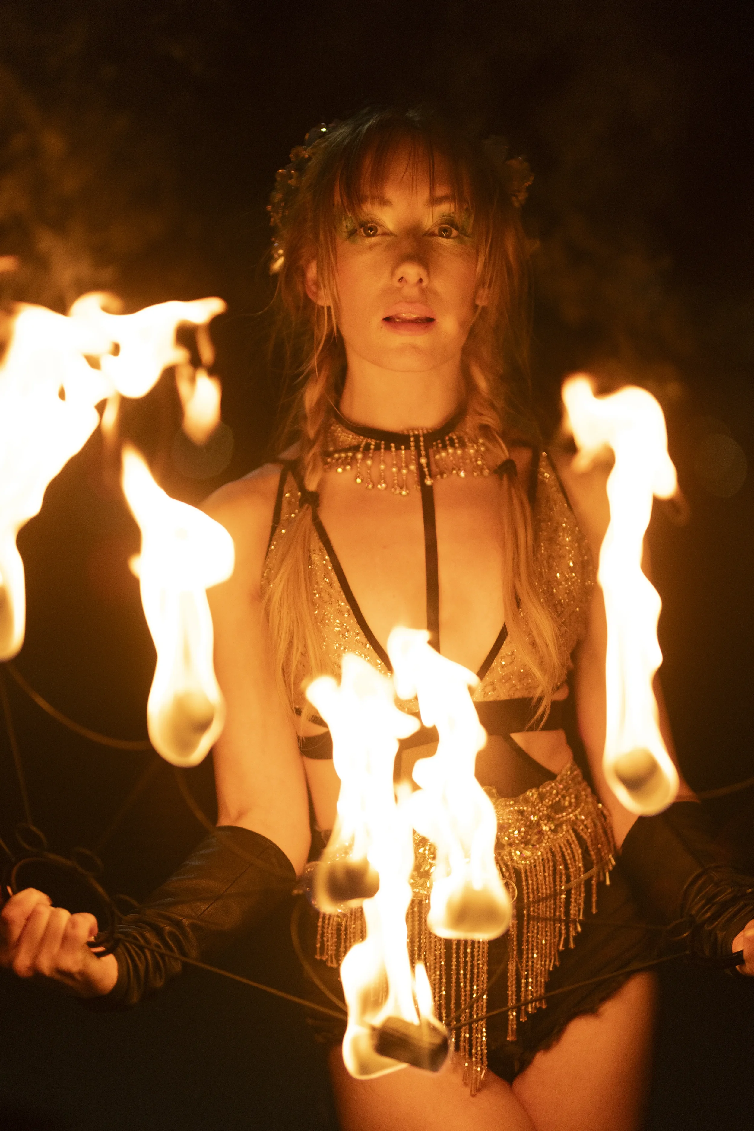 A woman performing a fire dance with flames surrounding her at night.