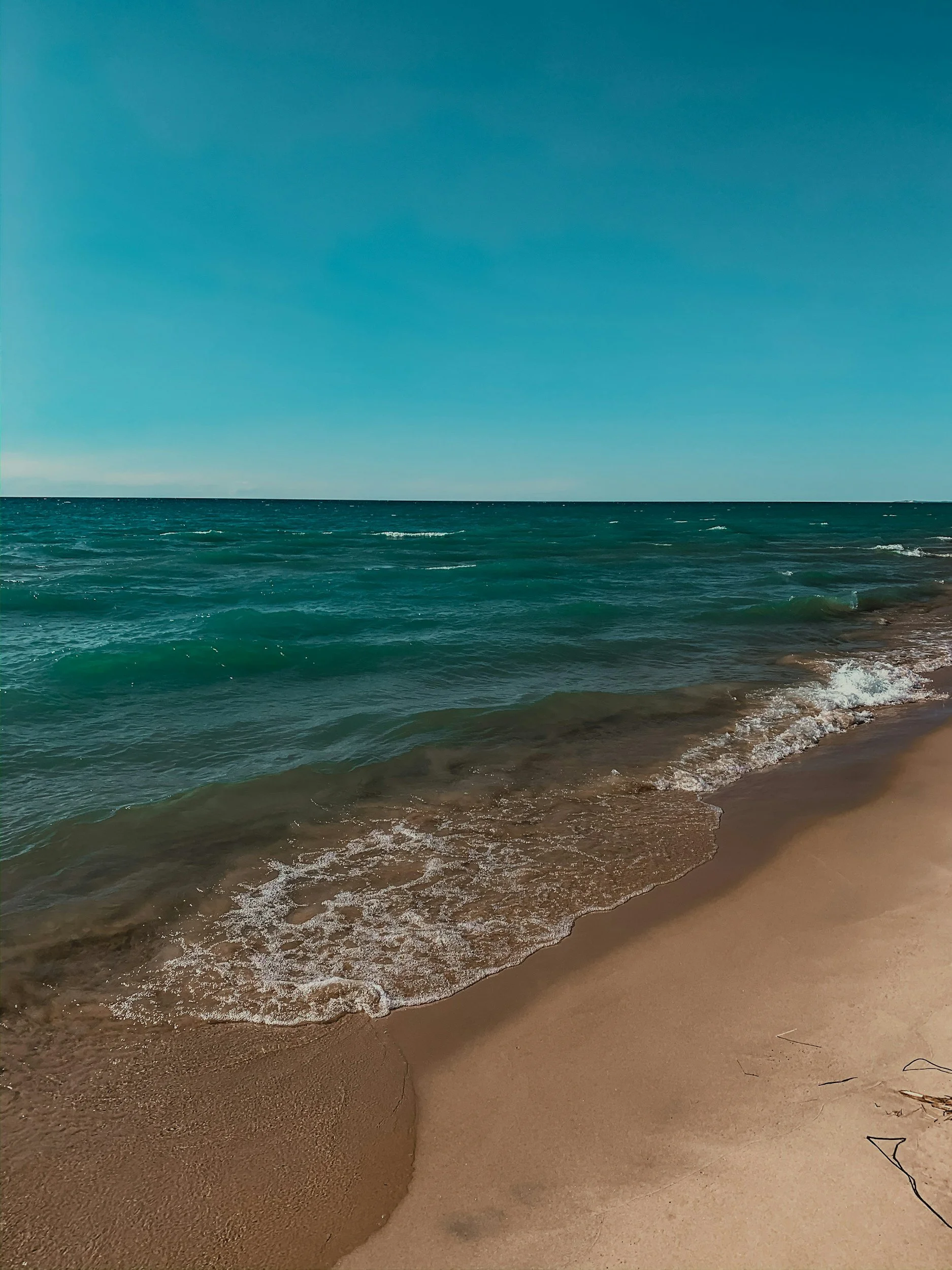 A sandy beach with gentle waves washing ashore under a clear blue sky.