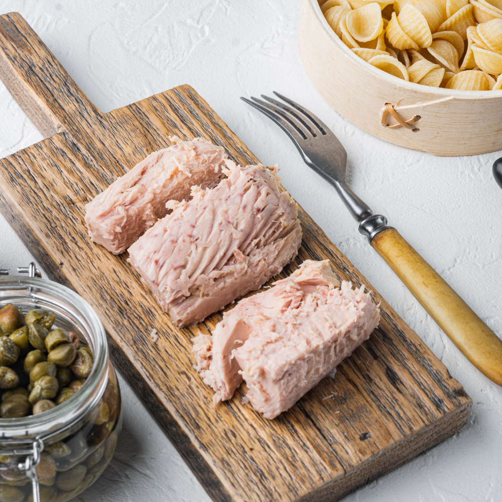 Flaking canned tuna with a fork in a mixing bowl for homemade tuna pasta salad.