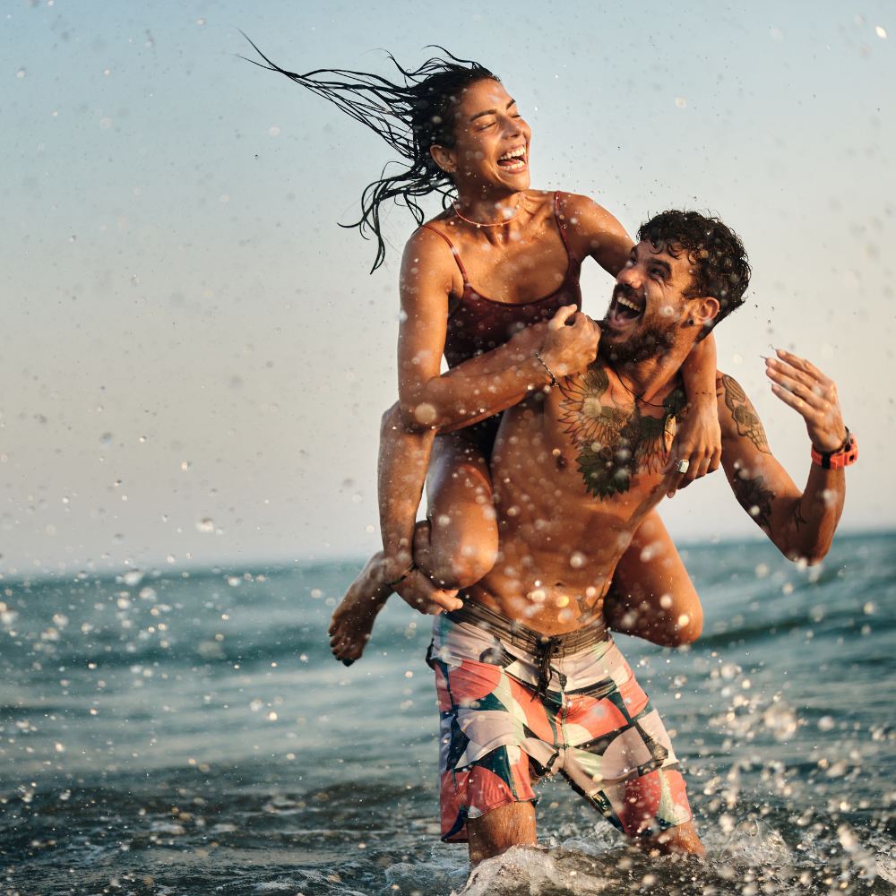 Romantic couple swimming together in the ocean during a warm summer sunset.