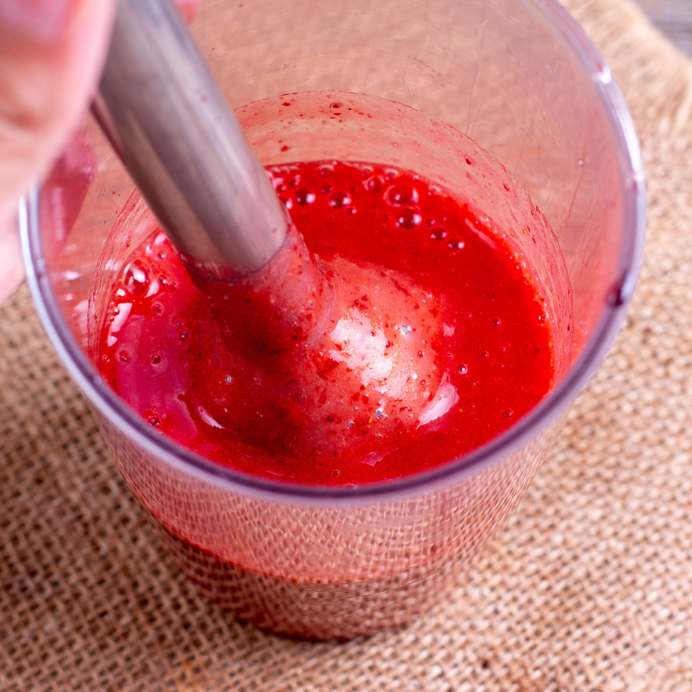 Immersion blender blending cooked strawberries into a smooth strawberry syrup for layered strawberry matcha latte
