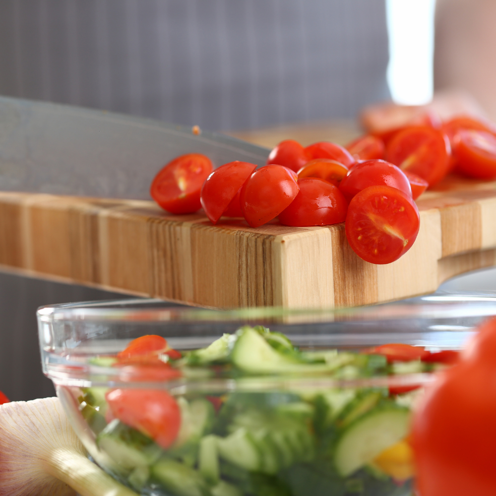 Chopping cucumbers, cherry tomatoes, and red onions on a cutting board for tuna pasta salad.