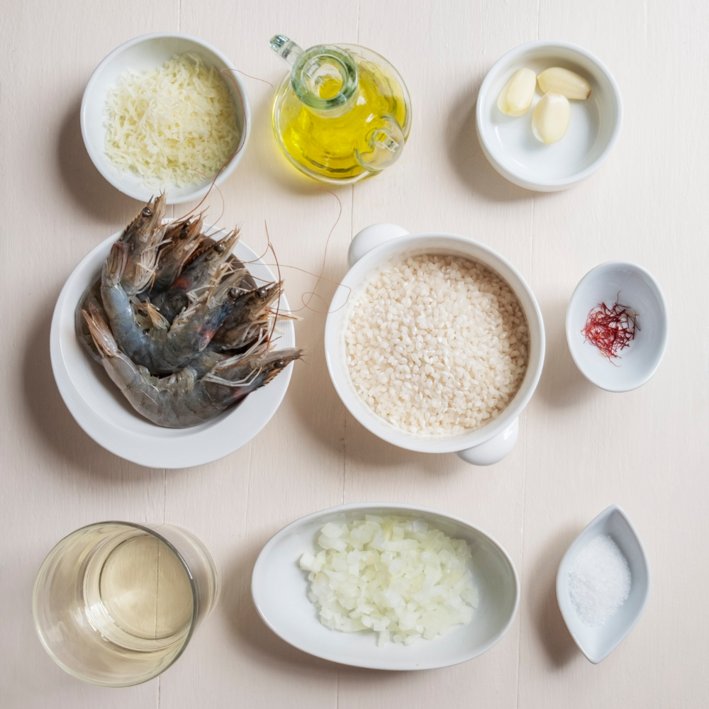 Overhead view of risotto ingredients including Arborio rice, shallots, garlic, seafood broth, Parmesan, and parsley