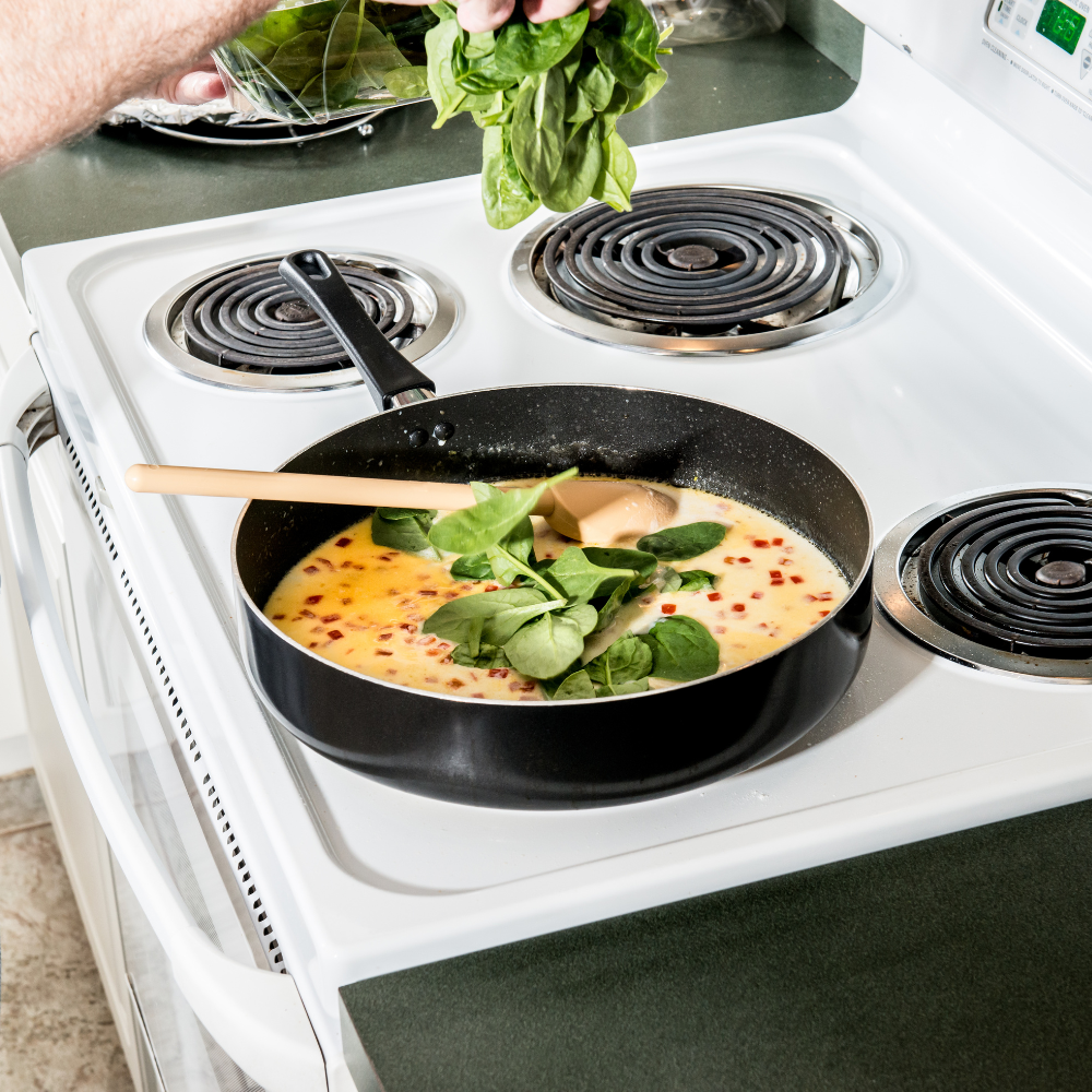 Cooked shrimp and fresh spinach being mixed into creamy orzo pasta in a skillet