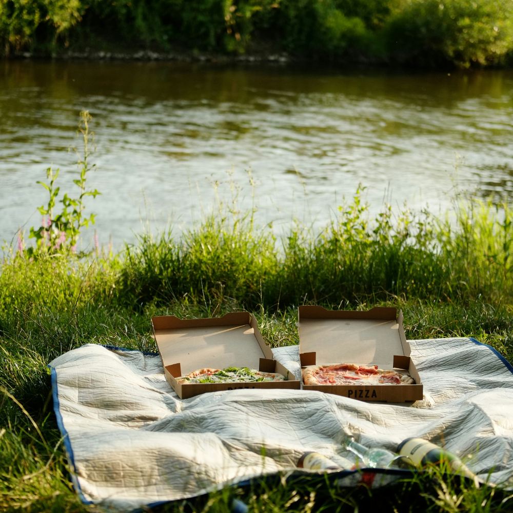 Friends enjoying a casual pizza picnic outdoors on a blanket with laughter and shared slices