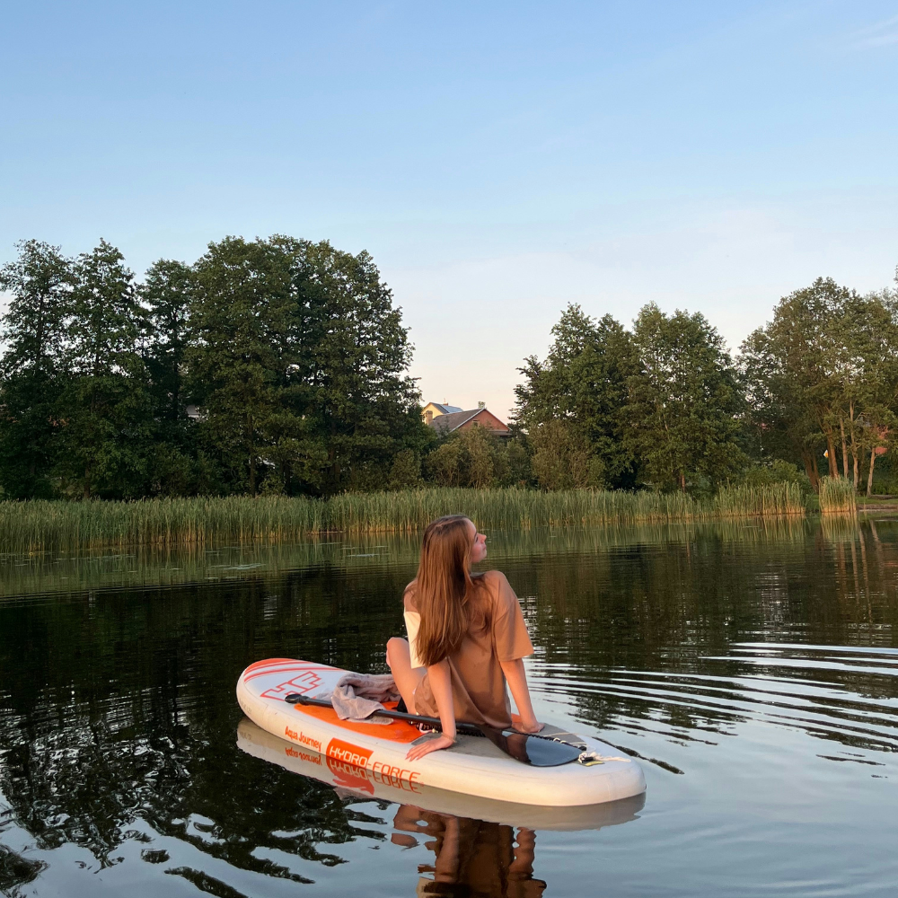 Woman paddleboarding on a calm lake during a sunny summer afternoon.