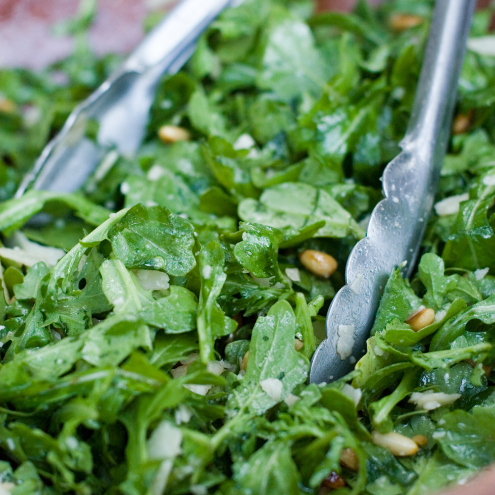 Tossing fresh arugula leaves with homemade anchovy vinaigrette for a crisp and simple arugula salad.