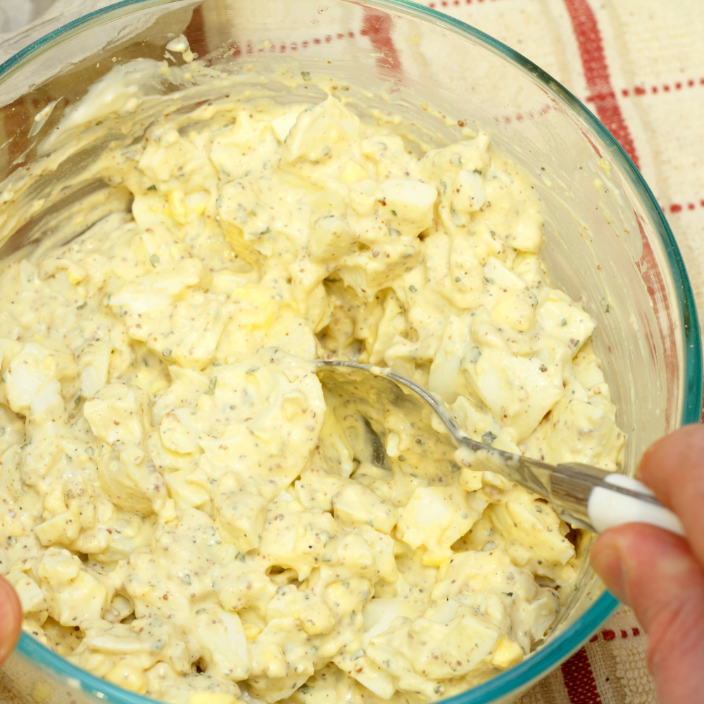 Gently folding soft-boiled eggs into creamy dressing to finish egg salad.