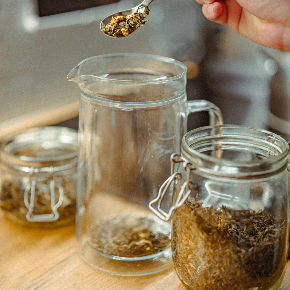 Measuring loose leaf tea into a glass jar before brewing iced tea.
