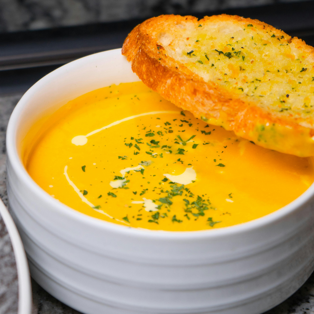 Bowl of creamy carrot ginger soup served with crusty bread on the side