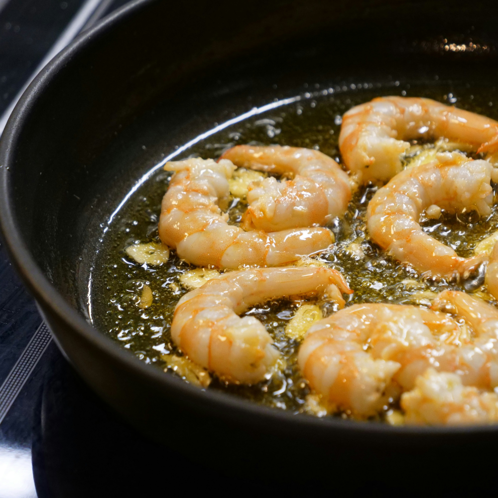 Shrimp sizzling in a hot skillet with olive oil and garlic, cooking until pink for a shrimp and orzo recipe