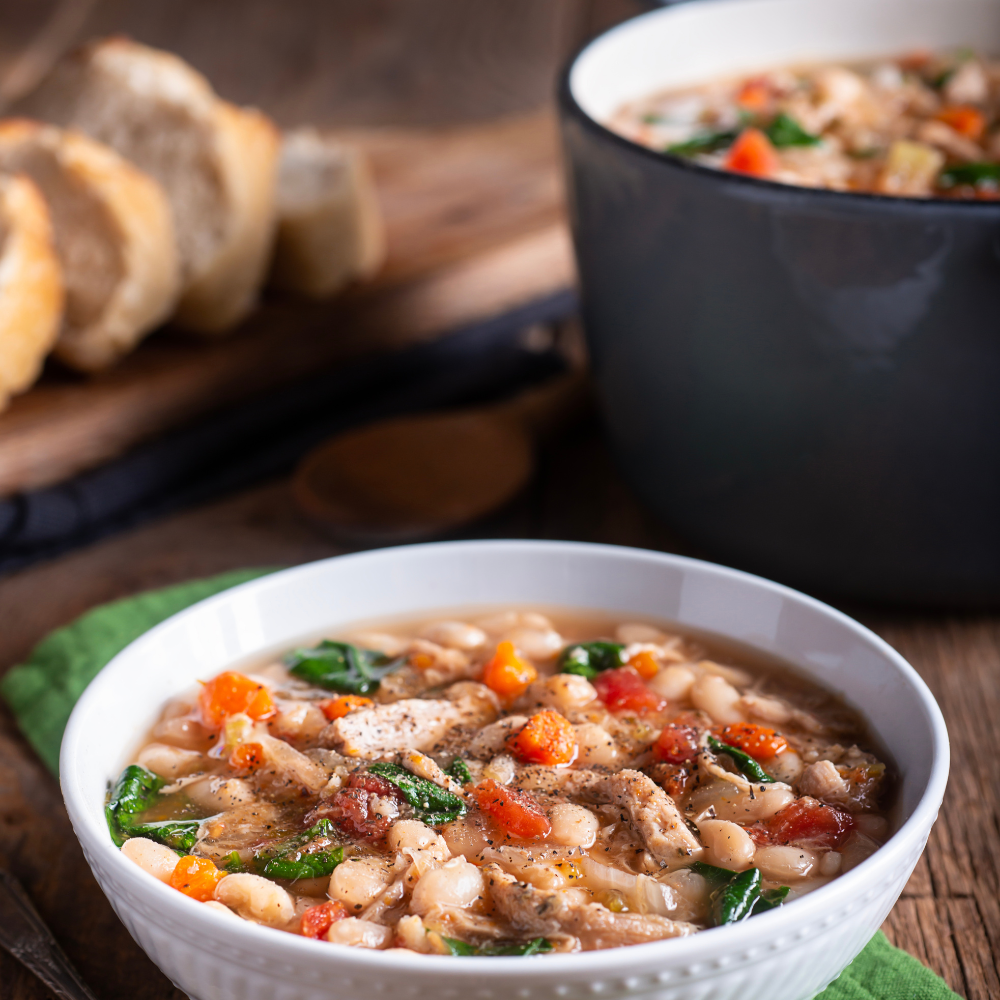 A bowl of homemade ham and bean soup ready to serve, garnished with parsley and accompanied by crusty bread