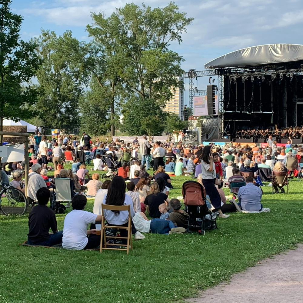Friends enjoying a live outdoor summer concert while sitting on blankets in the park.