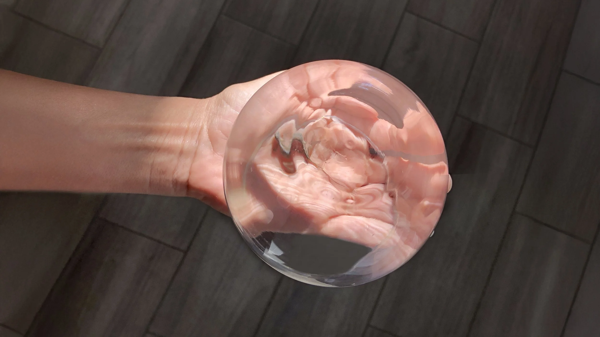 Caucasion hand holds clear glass ball in palm of hand, distorting the skin underneath