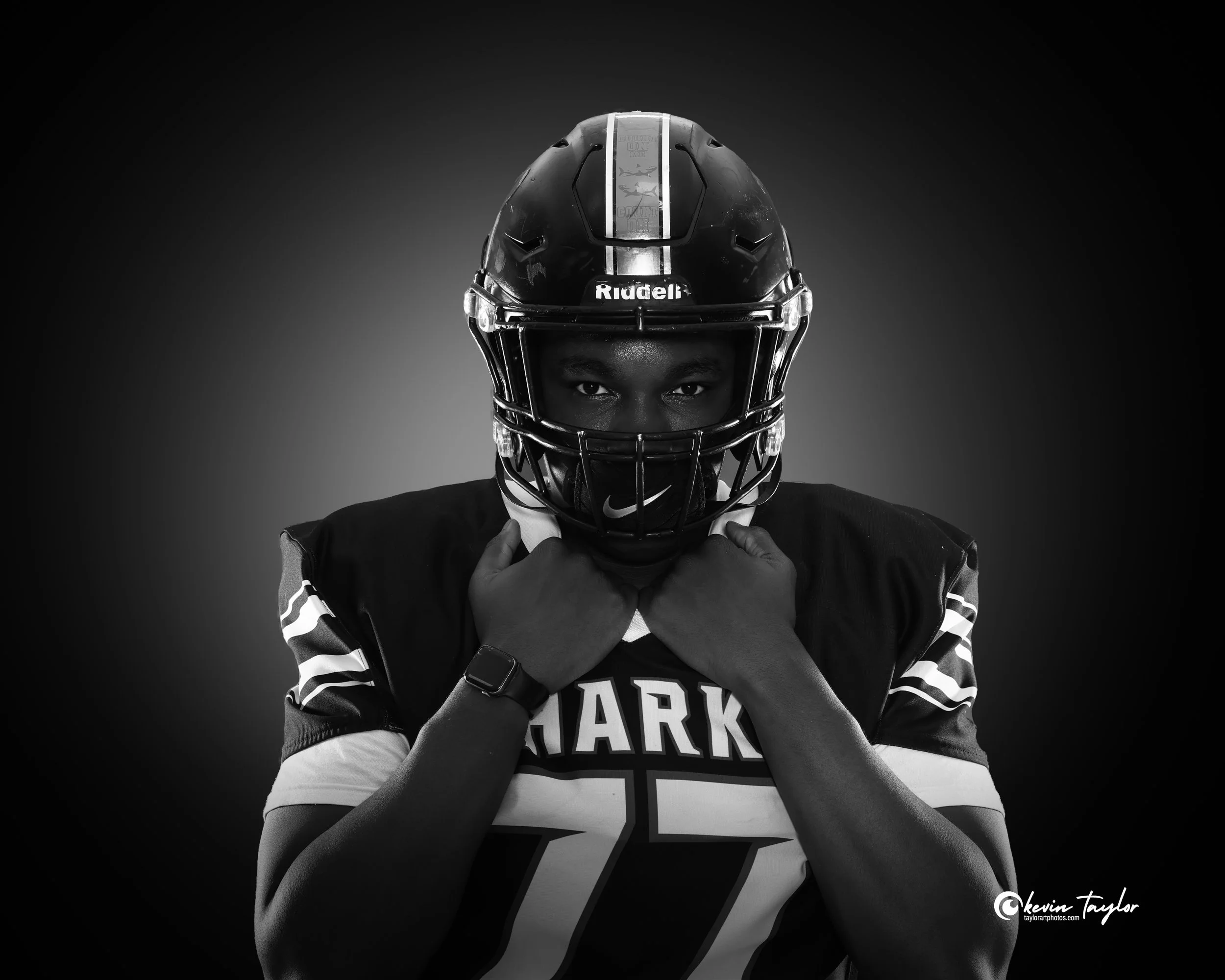 Football player wearing a helmet grips his jersey during a professional team media day portrait with dramatic studio lighting for athlete branding.