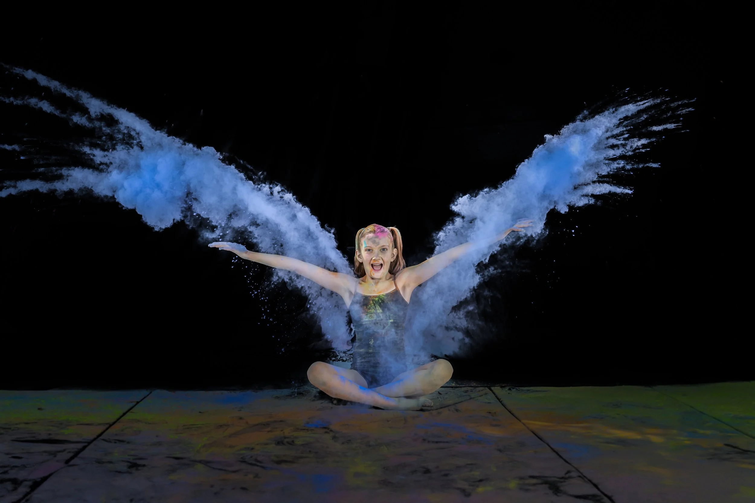 Professional color powder photography featuring a dancer creating dramatic blue powder wings during a creative portrait session