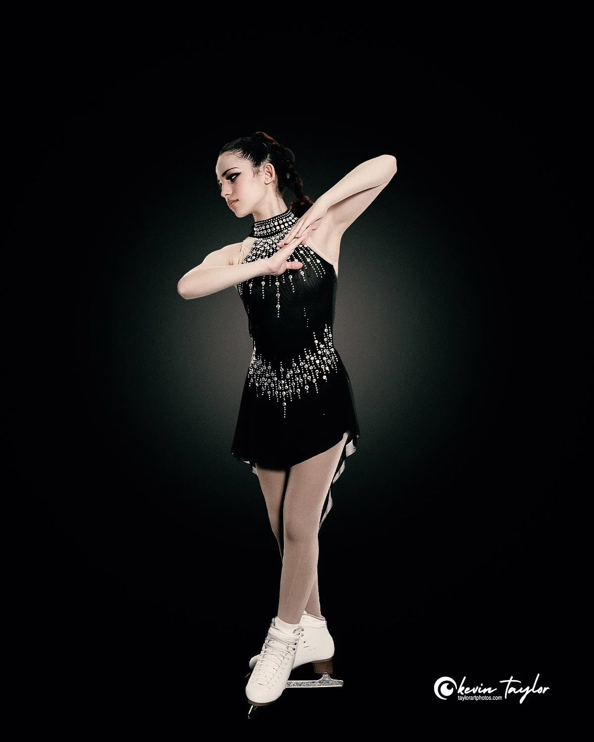 Competitive figure skater posing against a black backdrop for a professional portrait session.