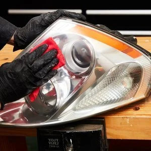 A person wearing black gloves cleaning or inspecting a car headlight with a red microfiber cloth.