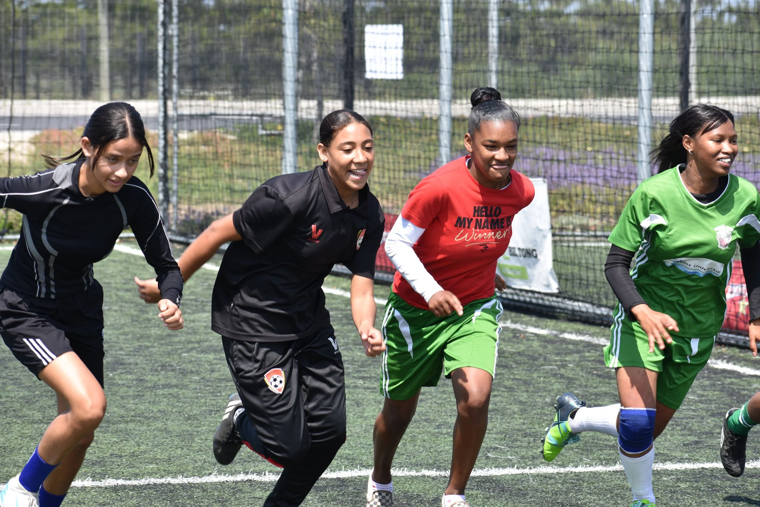  Four girls in soccer kits racing across a  soccer court.  