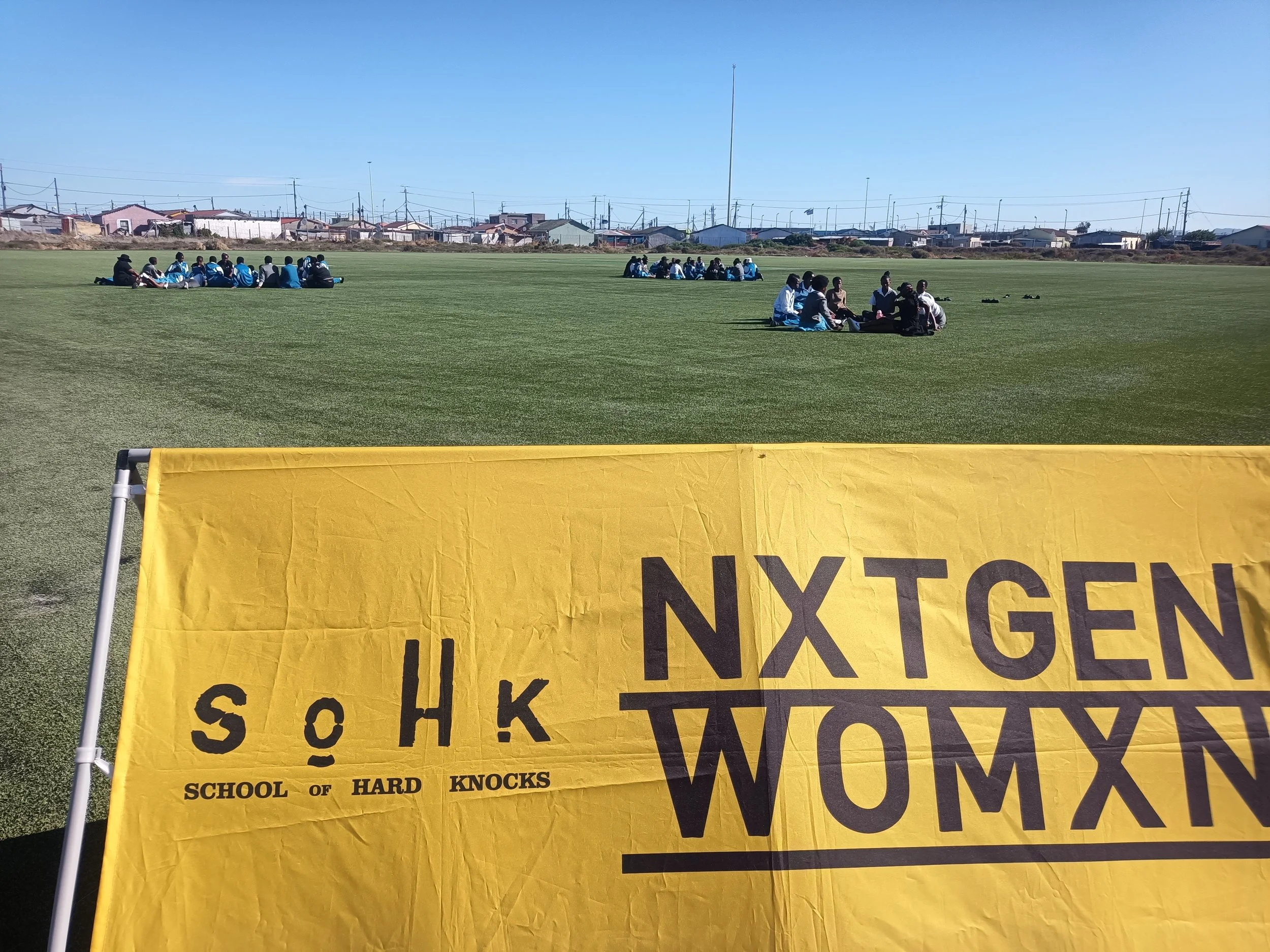  Yellow SoHK NxtGenWomxn banner on a sports field. 