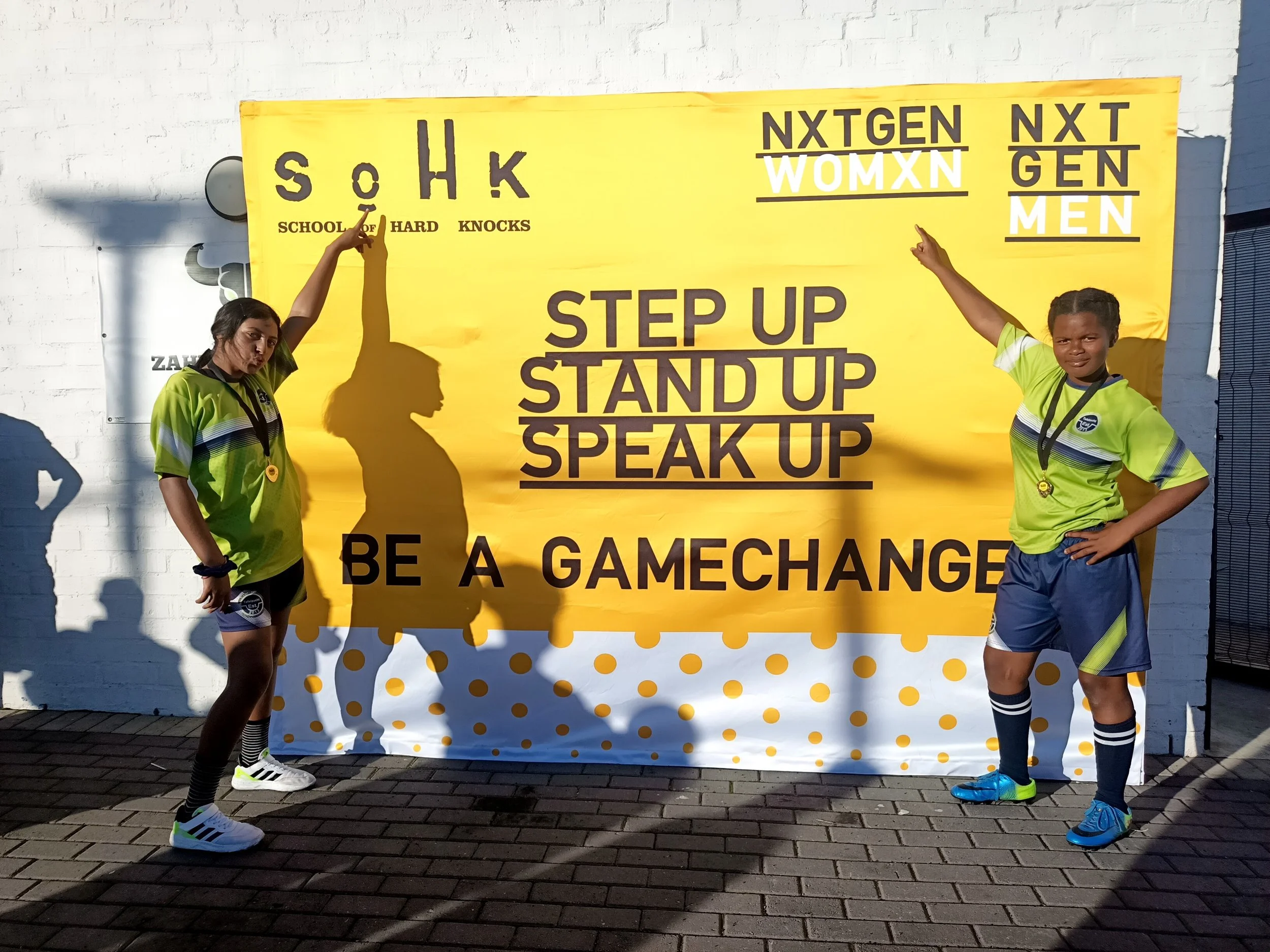  Two girls posing in front of a yellow "BE A GAMECHANGER" banner. 