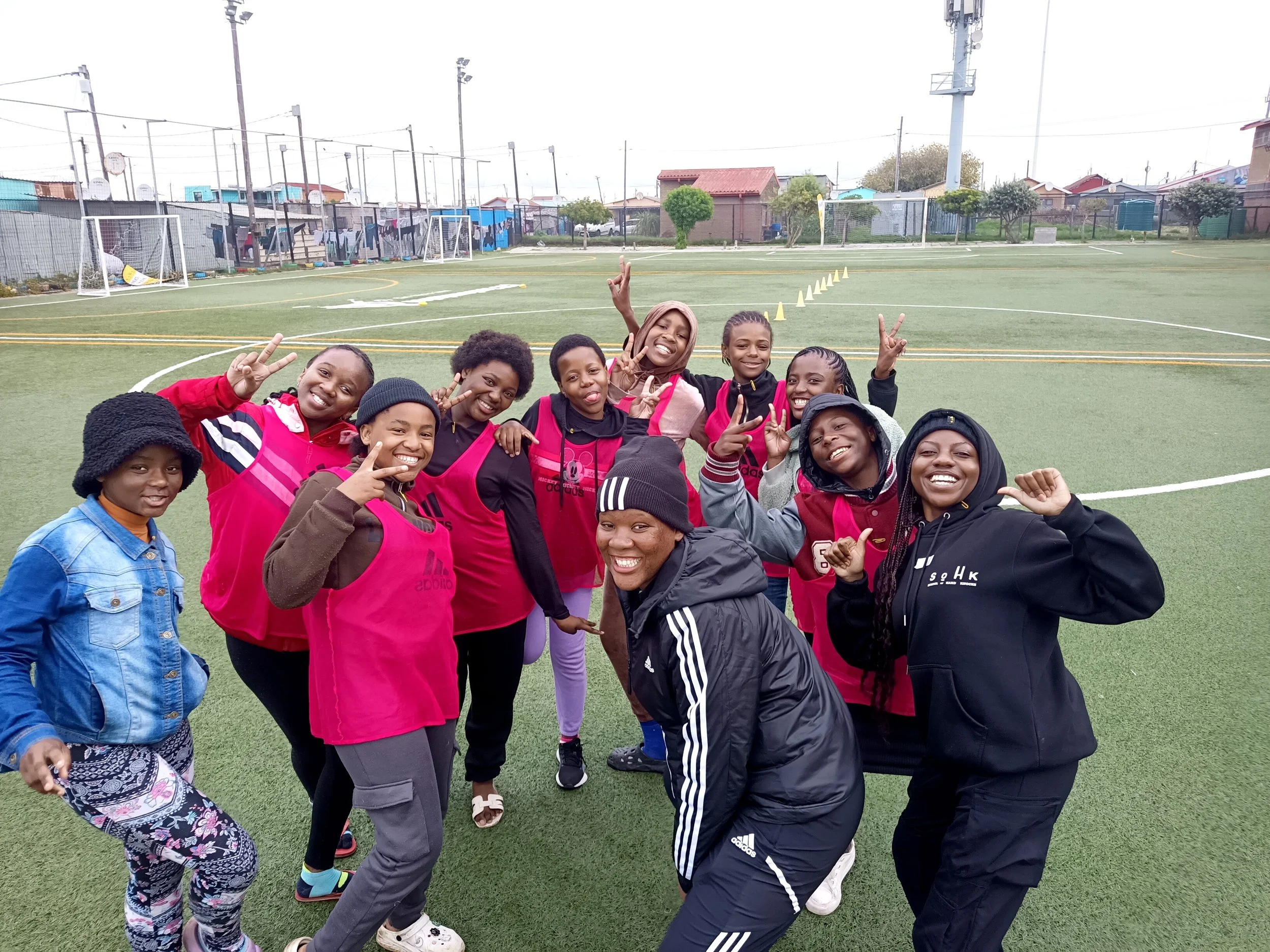  Group of girls and coach posing together and smiling on a field. 
