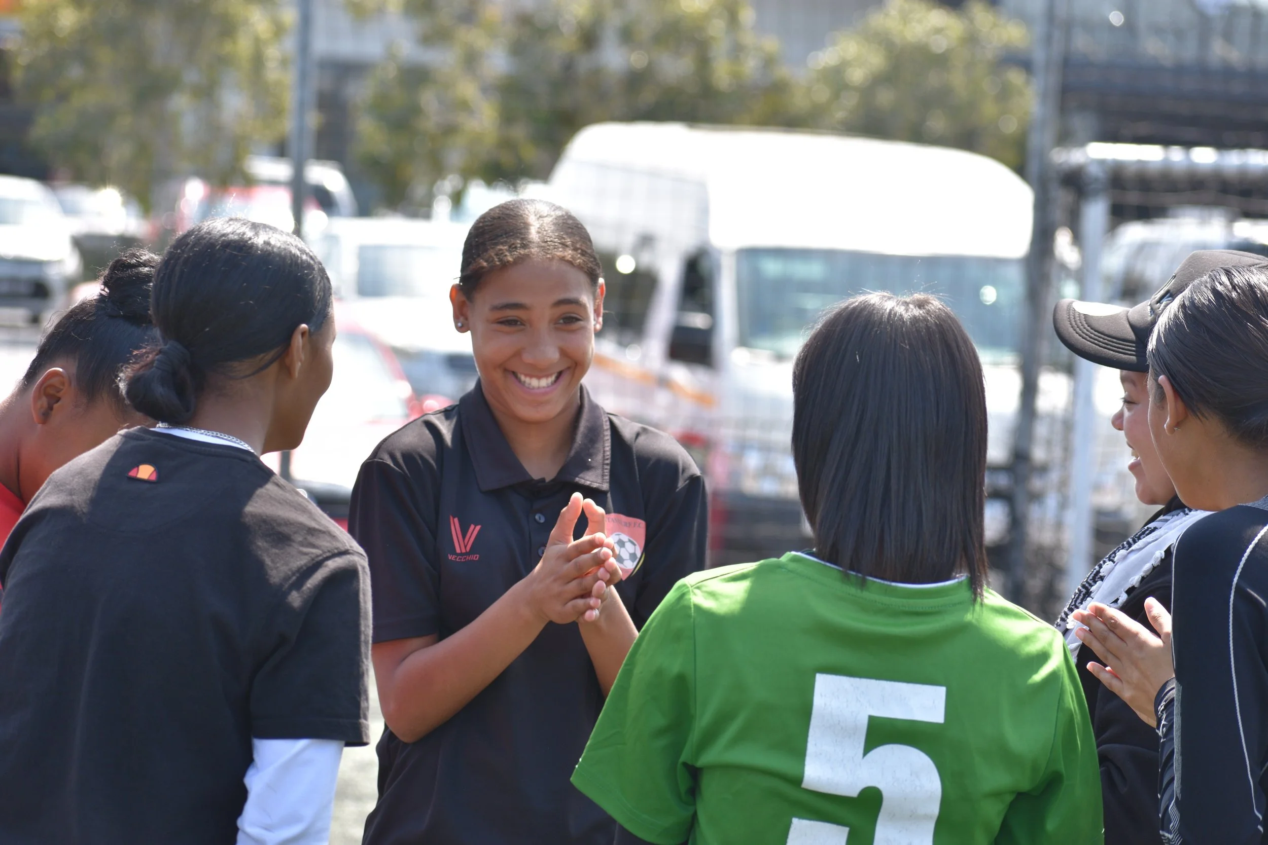  A young girl smiling and clapping while standing in a circle with other teammates. 