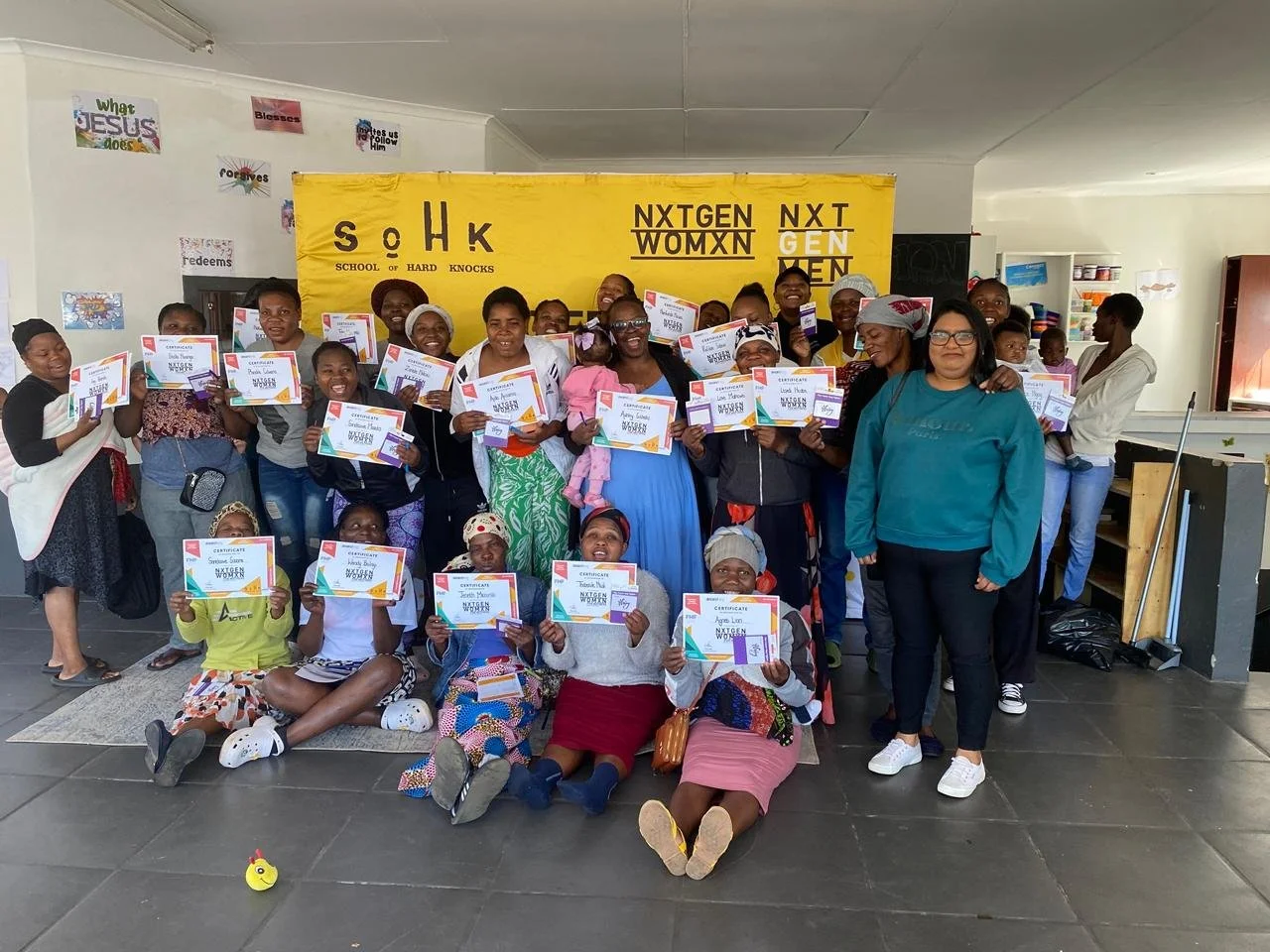  A group of participants posing with their certificates in front of a yellow SoHK banner at the graduation in Johannesburg. 