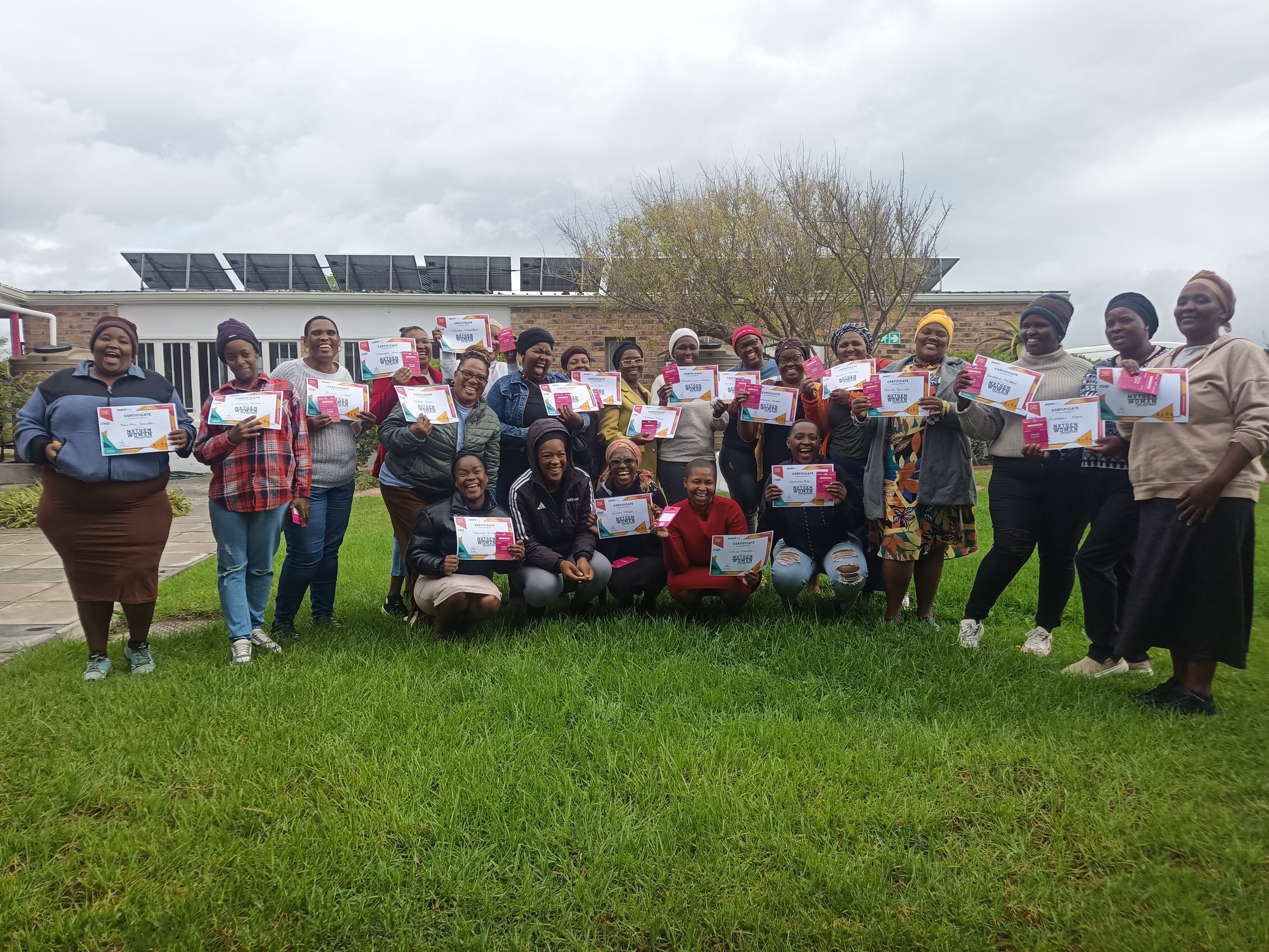  A group of participants posing together on a grassy field, holding up their certificates. 