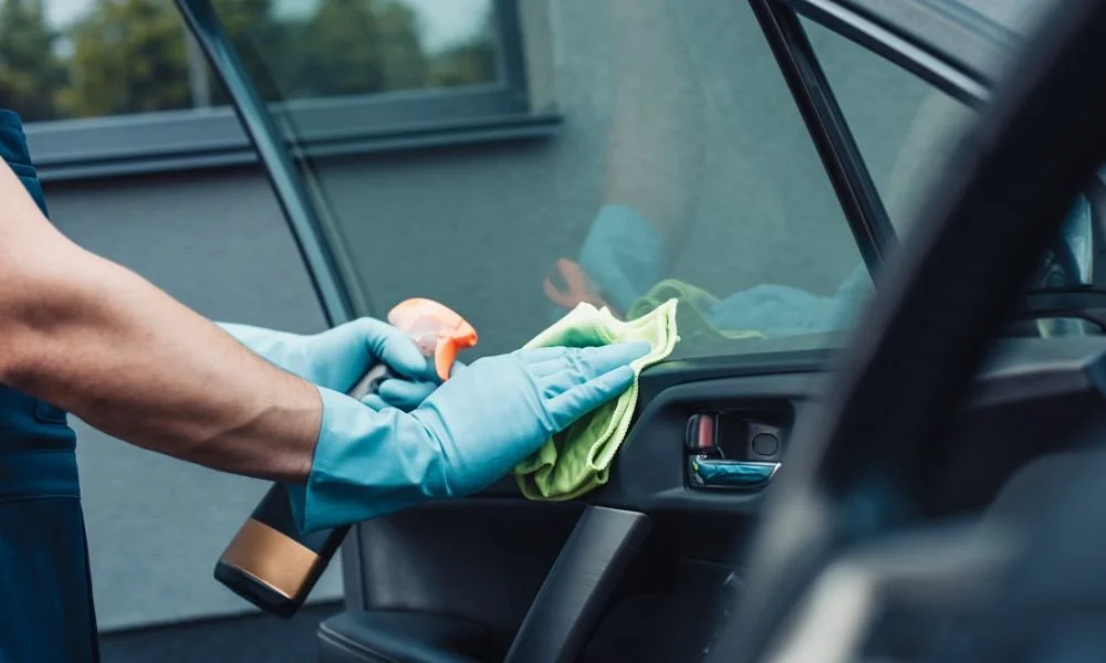 Person in blue gloves cleaning car interior with green cloth and spray bottle, emphasizing car detailing for improved resale value.