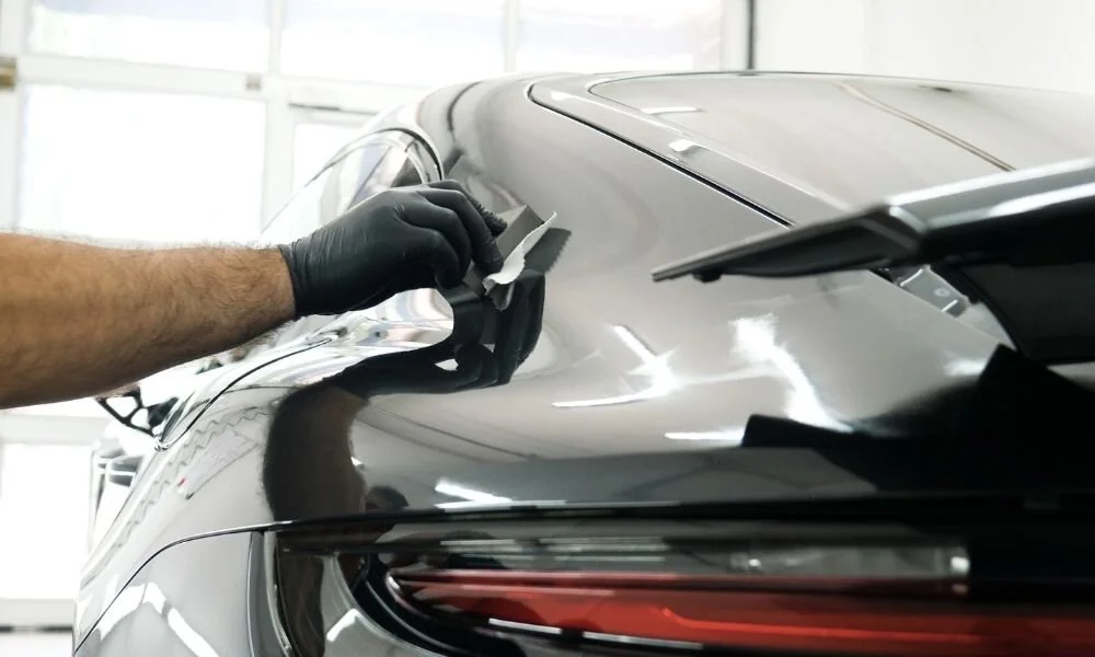 Person applying ceramic coating to a black vehicle's rear, showcasing auto detailing services by Owner's Pride.