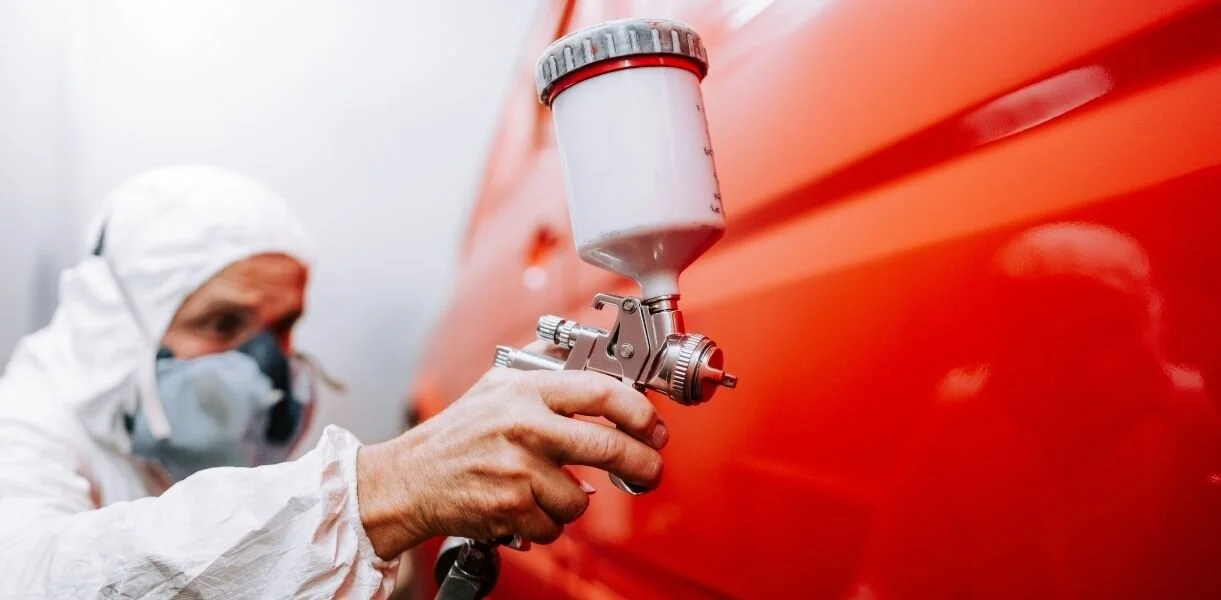 Person using a spray gun to apply red paint on a vehicle, demonstrating auto detailing techniques related to car remodeling and enhancement.