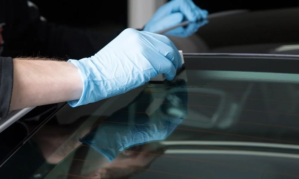 Person applying ceramic coating on a vehicle's surface, wearing blue gloves, emphasizing protective auto detailing service.