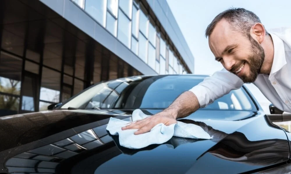Man polishing a black car hood with a microfiber cloth, showcasing vehicle maintenance and care, relevant to ceramic coating investment benefits.