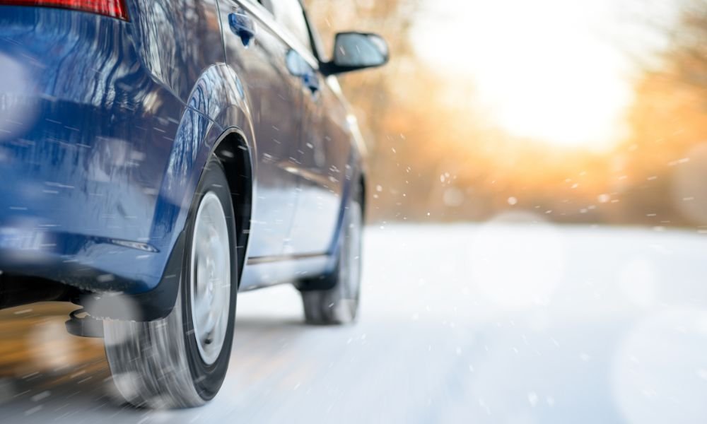 Blue car driving on snowy road in winter, emphasizing the importance of maintaining car exterior during harsh weather conditions.