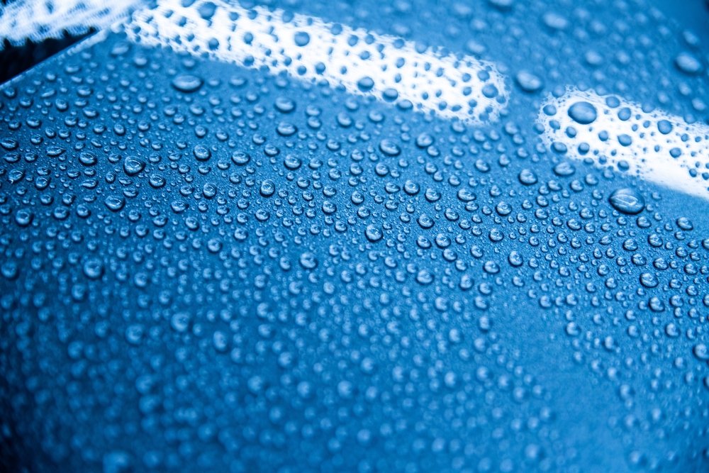 Close-up of water droplets on a blue car surface, illustrating the hydrophobic properties of ceramic coating, relevant to vehicle protection in Omaha's climate.