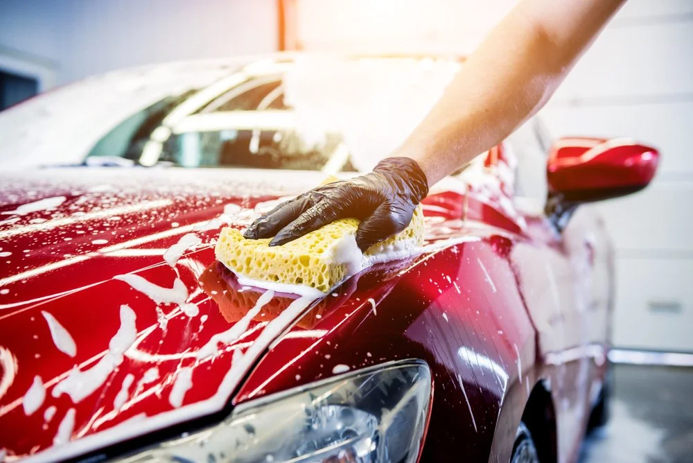 Person cleaning a red car with a sponge, showcasing vehicle maintenance after PPF installation in Omaha, NE.