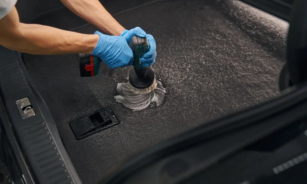 Detailing technician using a power scrubber to clean vehicle carpet, emphasizing professional car detailing services for maintaining vehicle value.