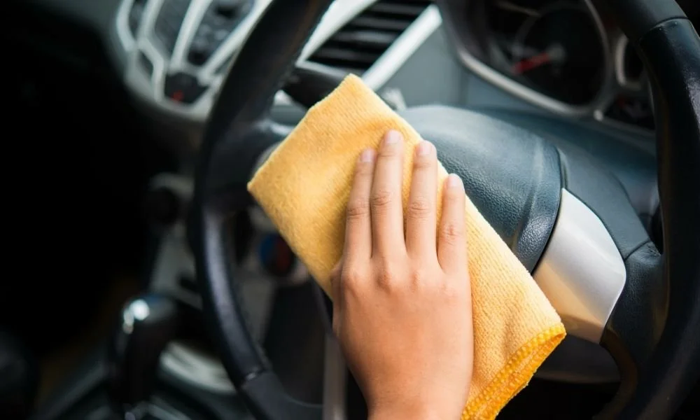 Hand cleaning a car steering wheel with a yellow microfiber cloth, emphasizing vehicle preparation for detailing services.