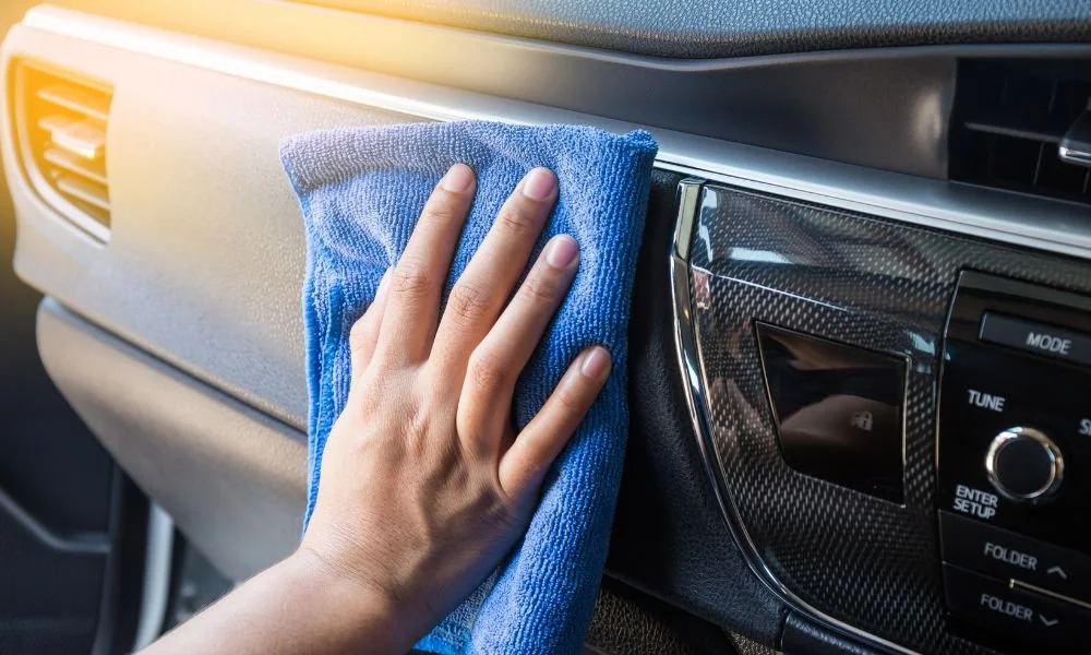 Hand cleaning the dashboard of a car with a microfiber cloth, emphasizing the importance of interior detailing before summer.