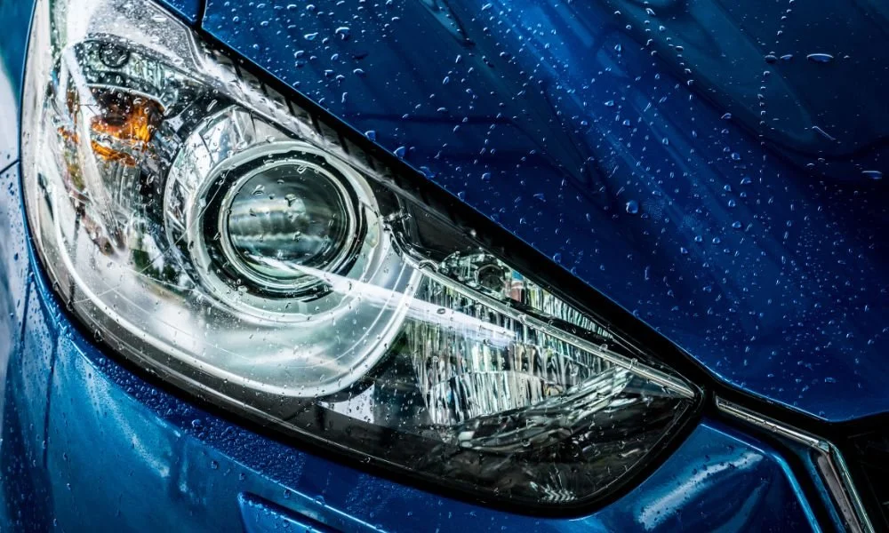 Close-up of a blue car's headlight with water droplets, emphasizing the importance of car washes during winter to maintain vehicle exterior.