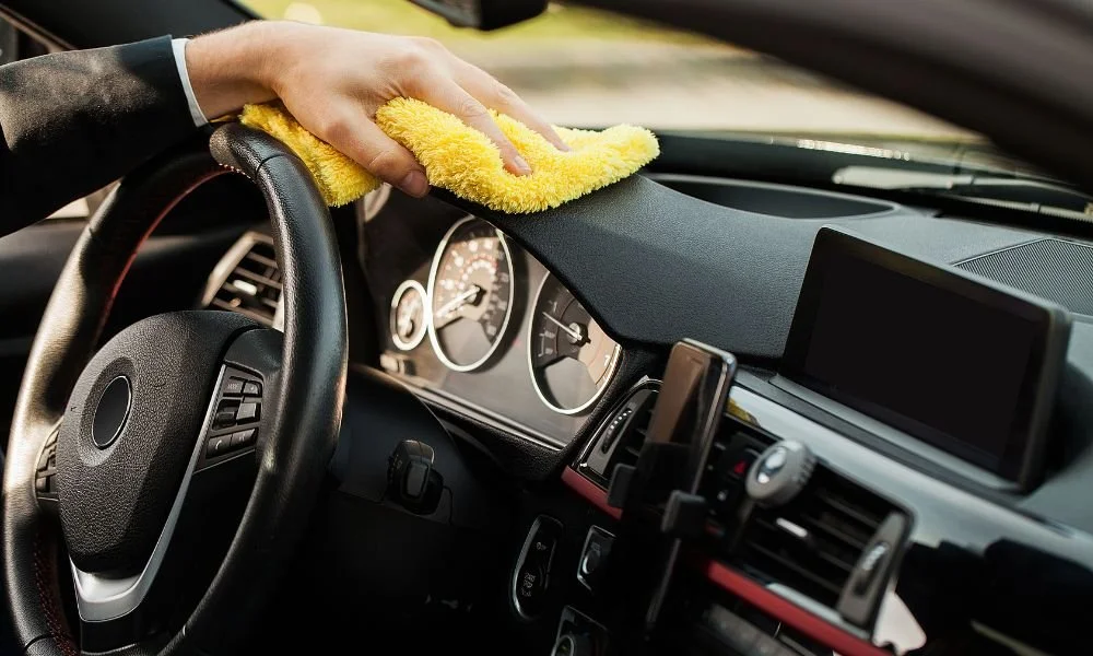 Person using a microfiber cloth to clean the dashboard of a car, highlighting the interior detailing process for vehicle maintenance and enhancement.
